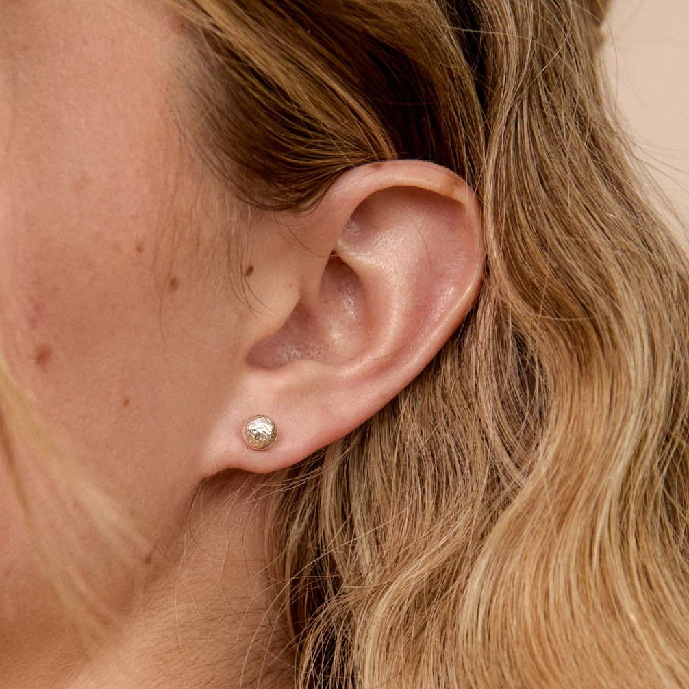 close up of a blonde woman's ear wearing a 9ct gold pebble stud earring