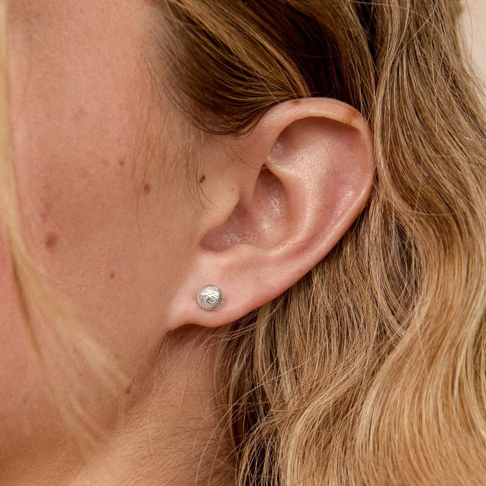 A close-up side view of a blonde woman's ear wearing a silver pebble stud