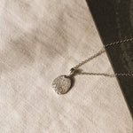silver pendant necklace with dog nose print texture against a beige fabric