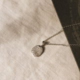 silver pendant necklace with dog nose print texture against a beige fabric