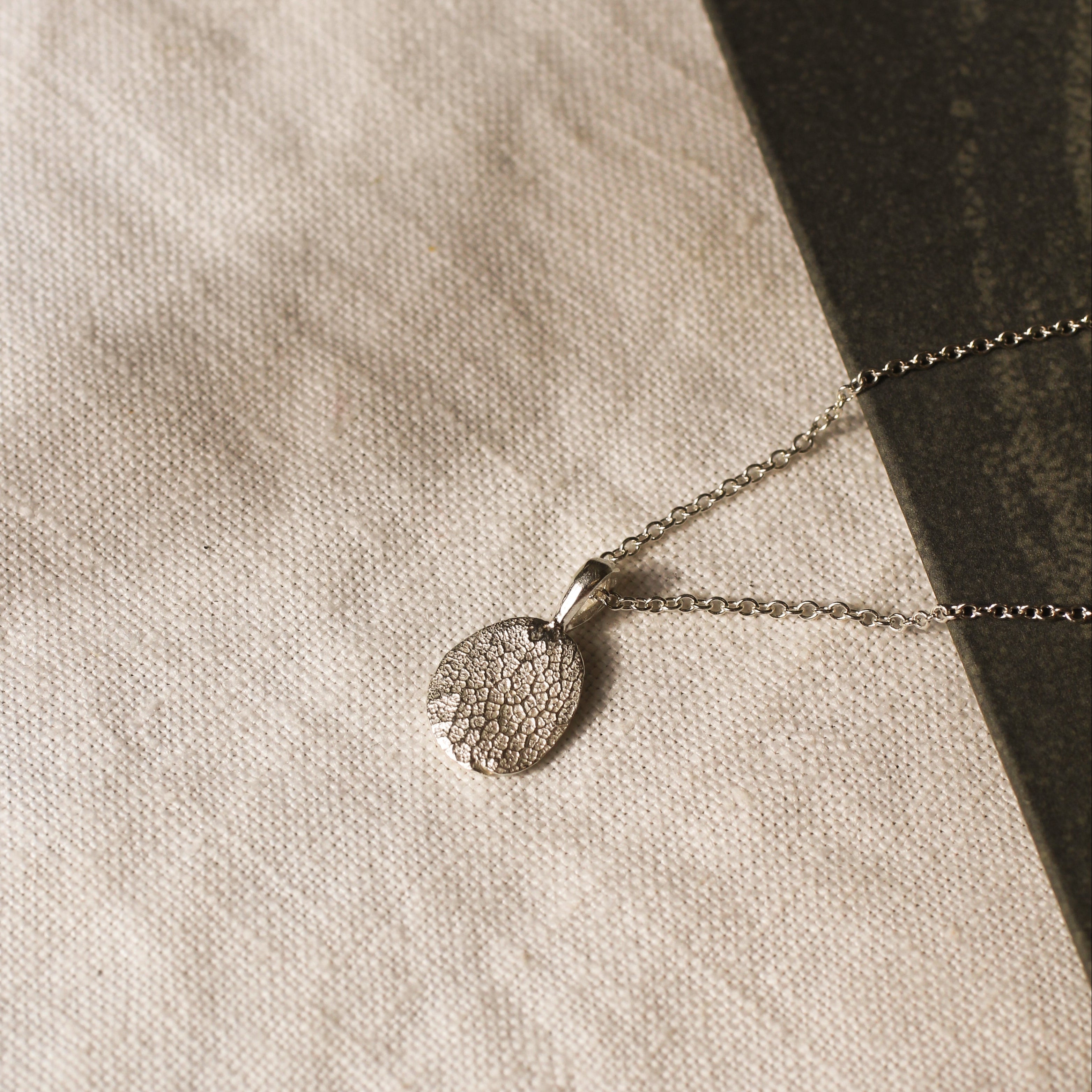 silver pendant necklace with dog nose print texture against a beige fabric