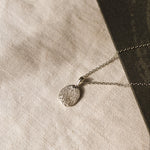 silver pendant necklace with dog nose print texture against a beige fabric