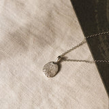 silver pendant necklace with dog nose print texture against a beige fabric