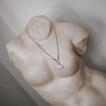 silver chunky necklace with round textured pendant on a marble statue