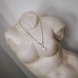 silver chunky necklace with round textured pendant on a marble statue