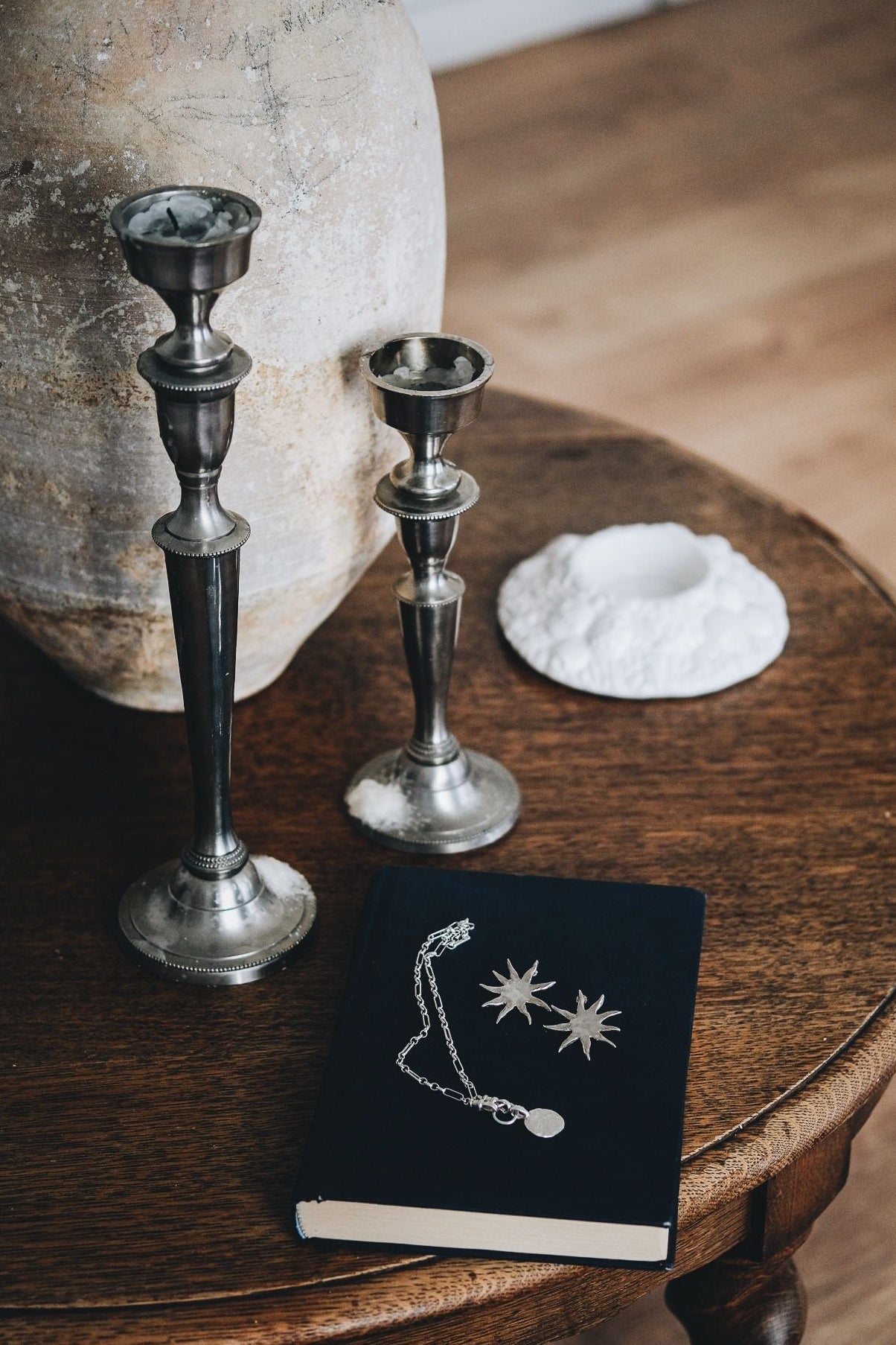 Decorative items including silver candlesticks and a black book with jewelry design on a wooden table.