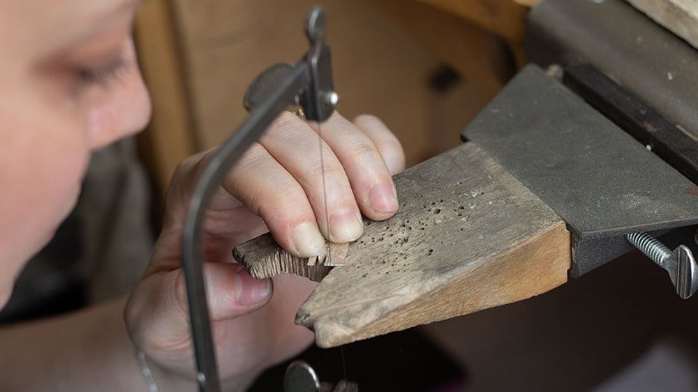Person using a hand saw on a piece of metal on a jewellery work bench.