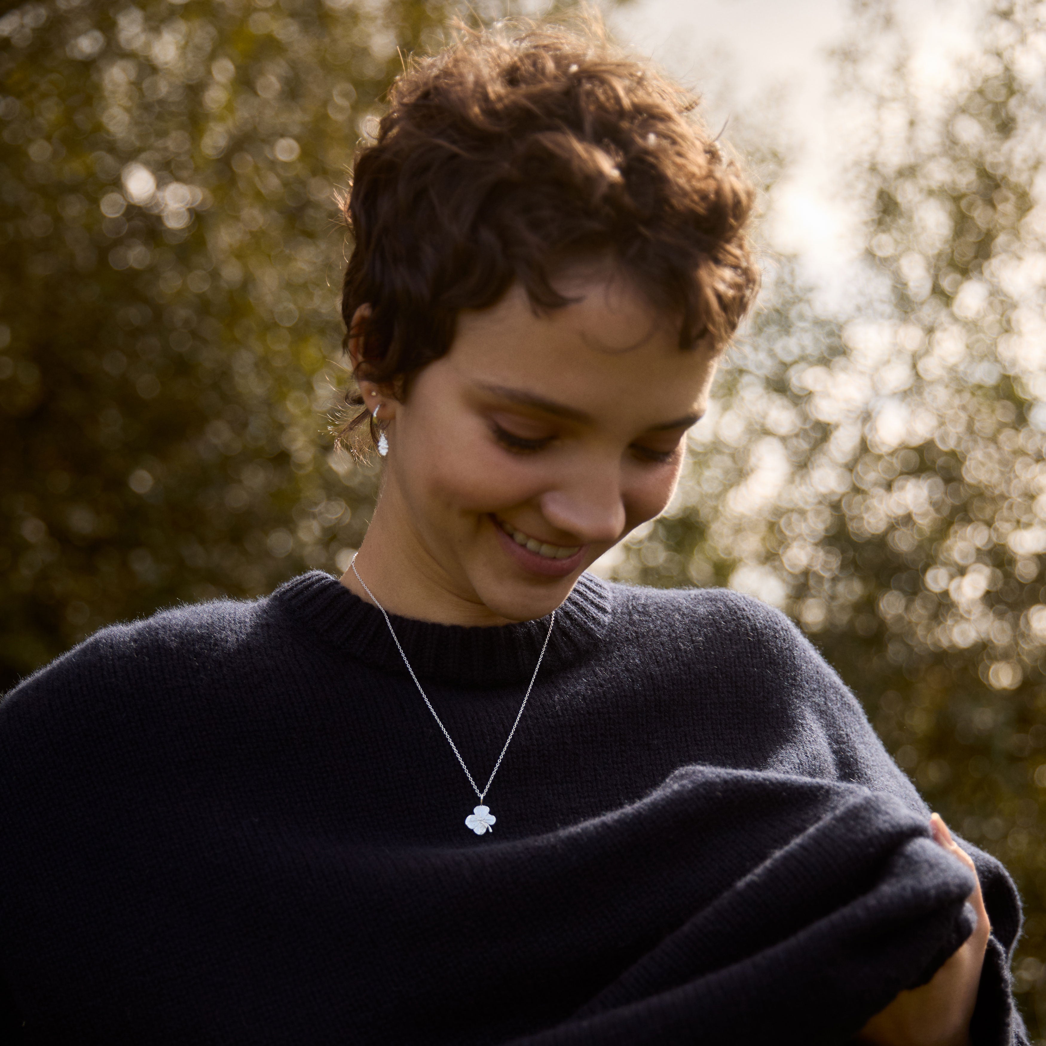 Woman wearing a dark sweater and necklace with a blurred natural background