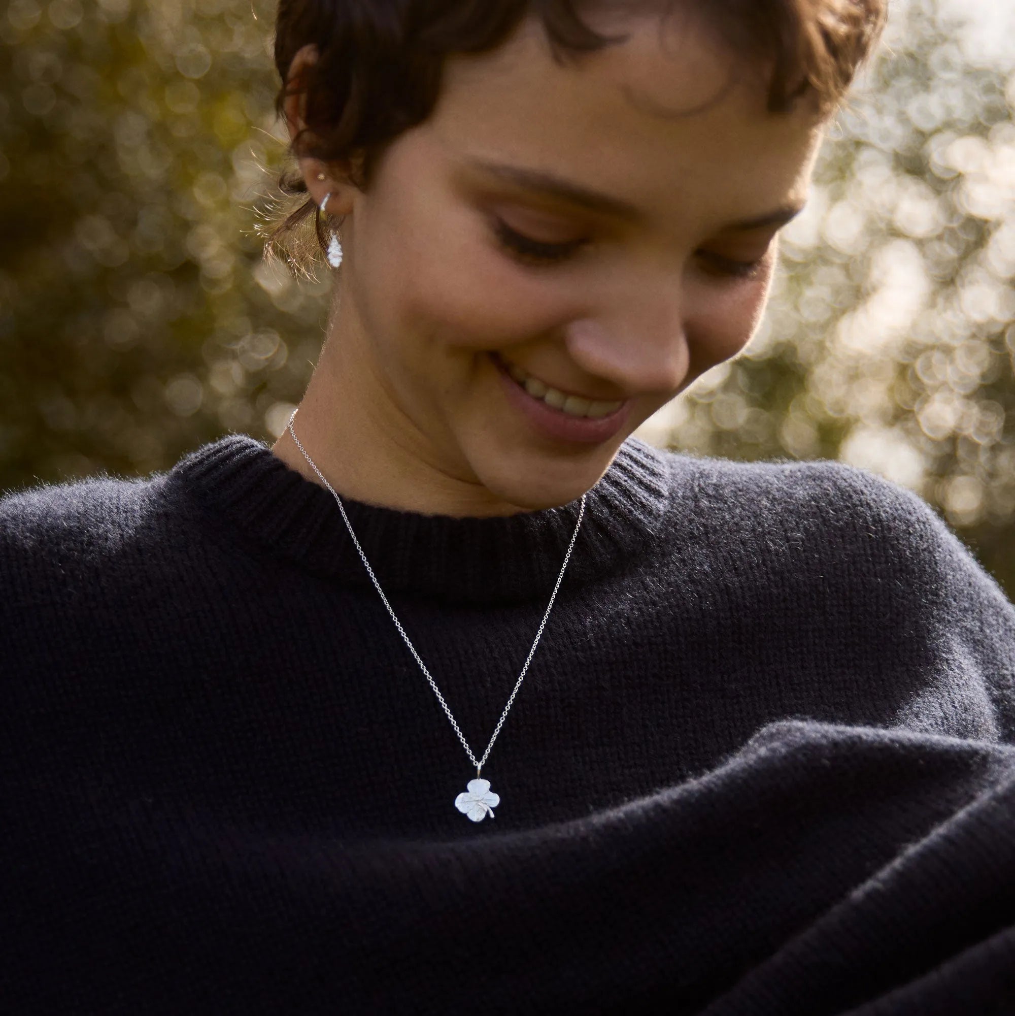 Woman wearing a necklace with a clover pendant outdoors