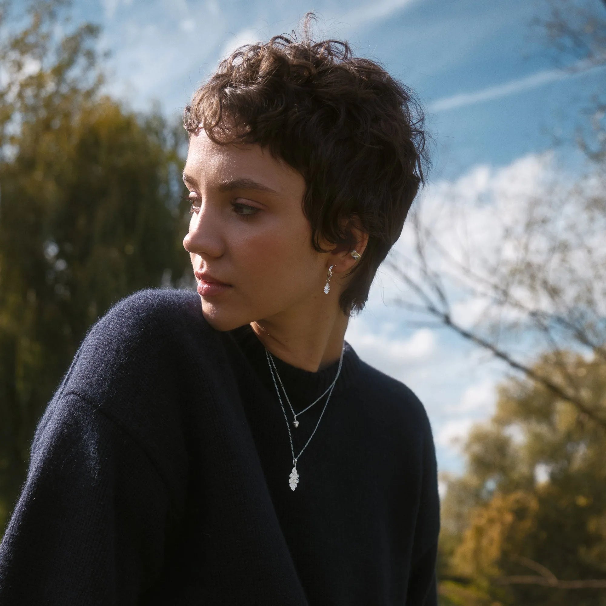Woman with short hair wearing silver jewellery, a navy jumper and necklace outdoors