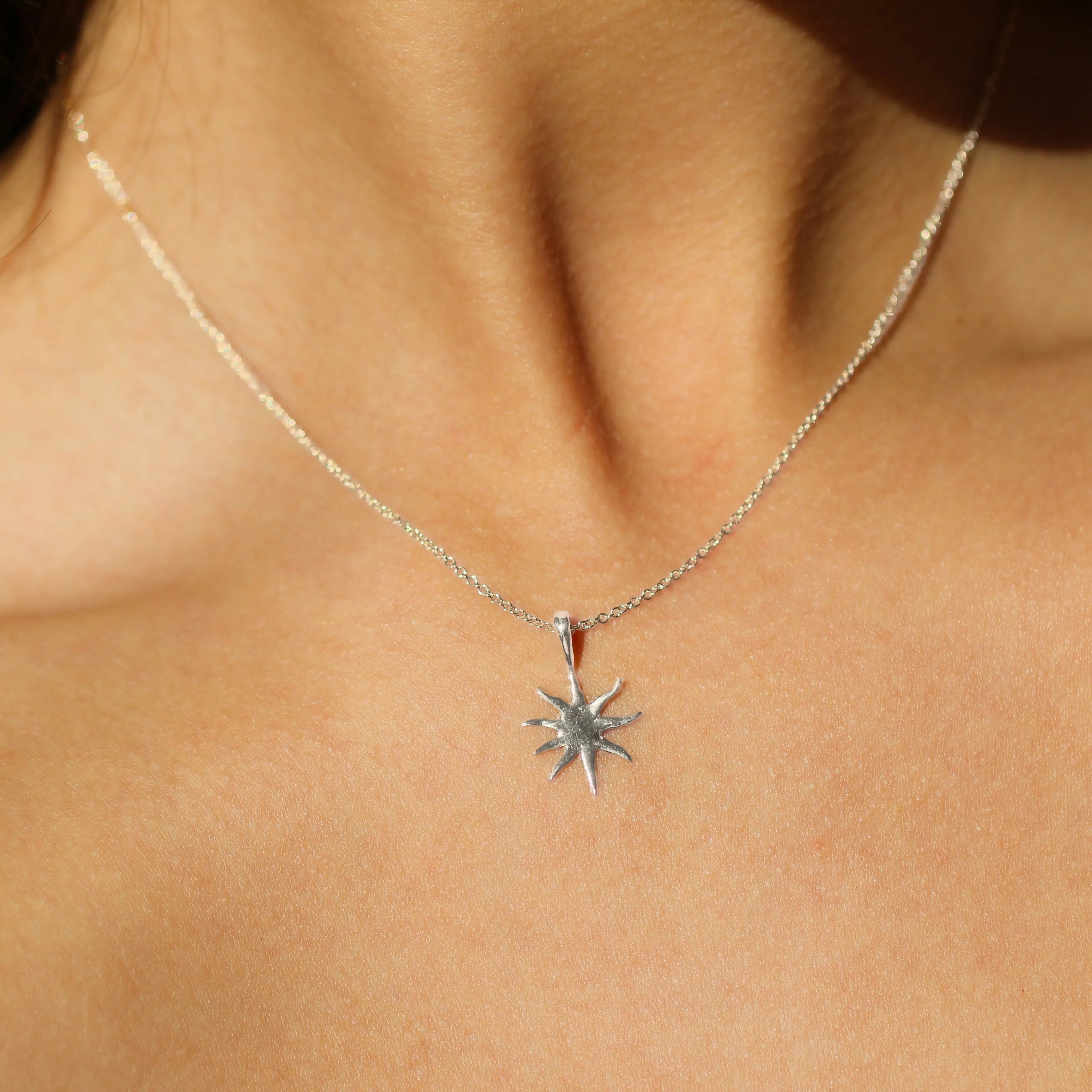 close up of person wearing a silver mini sun pendant necklace in the sun