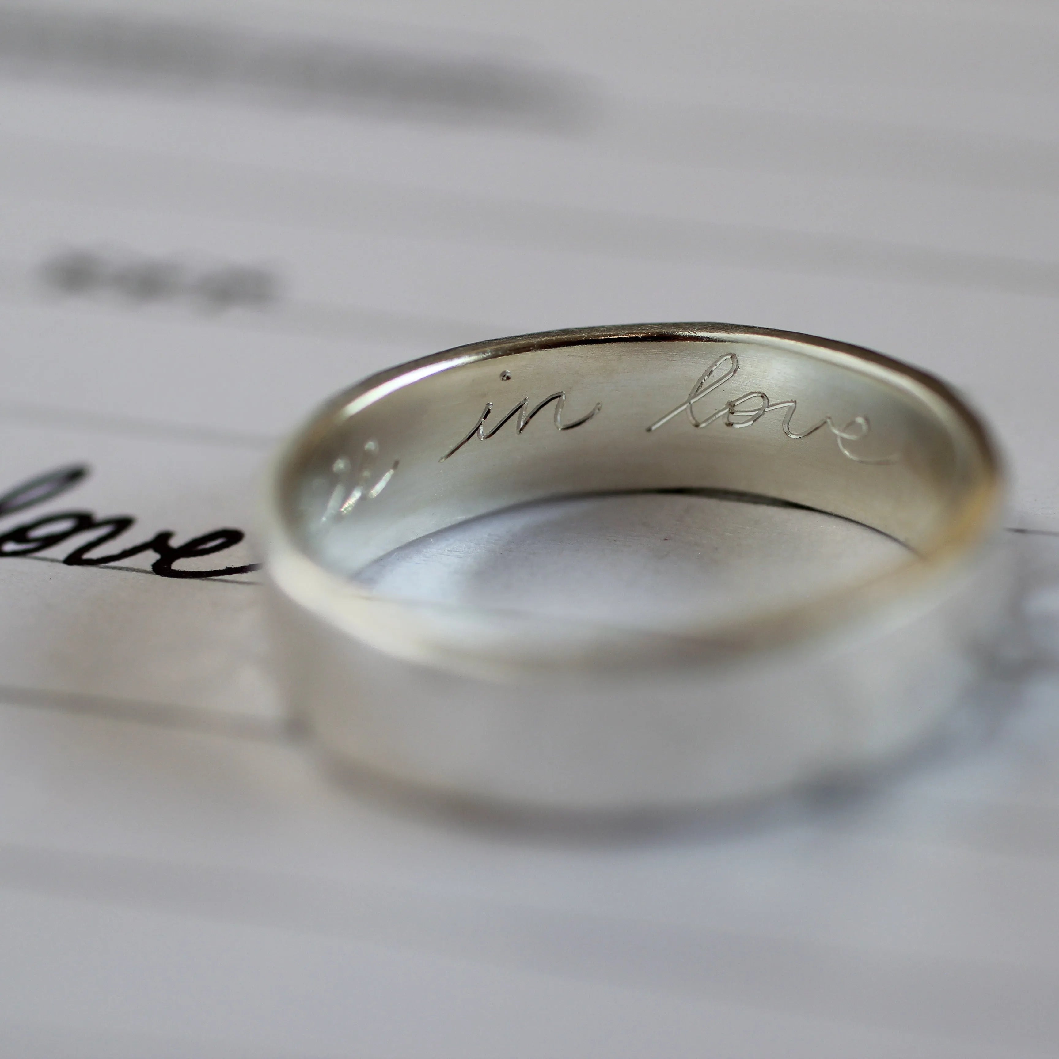 silver ring with engraving 'in love' with handwritten word 'love' with blurred foreground