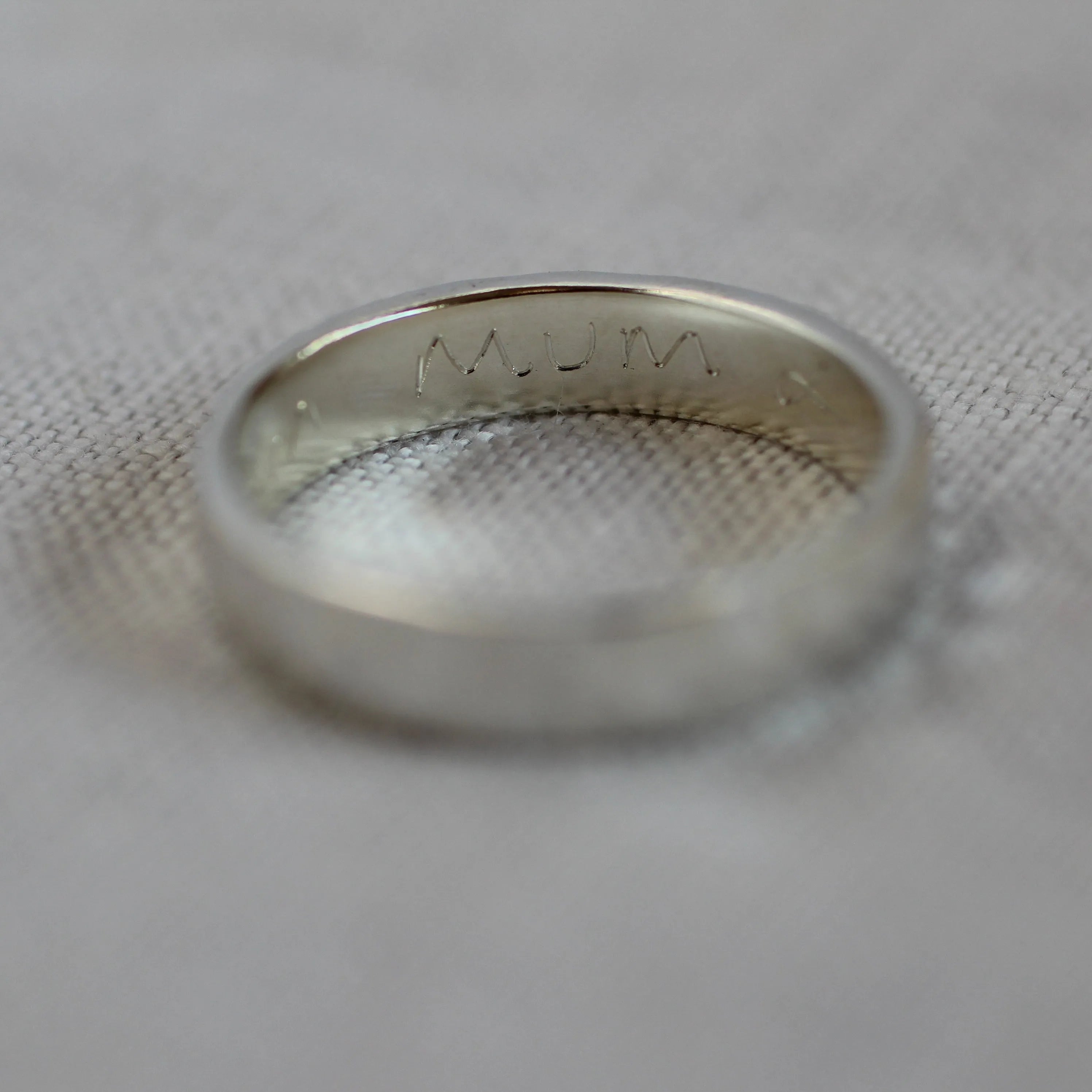 4mm silver ring with the handwritten word 'mum' engraved on the inside with blurred foreground