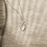 Silver leaf-shaped pendant on a beige fabric background