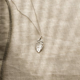 Silver leaf-shaped pendant on a beige fabric background