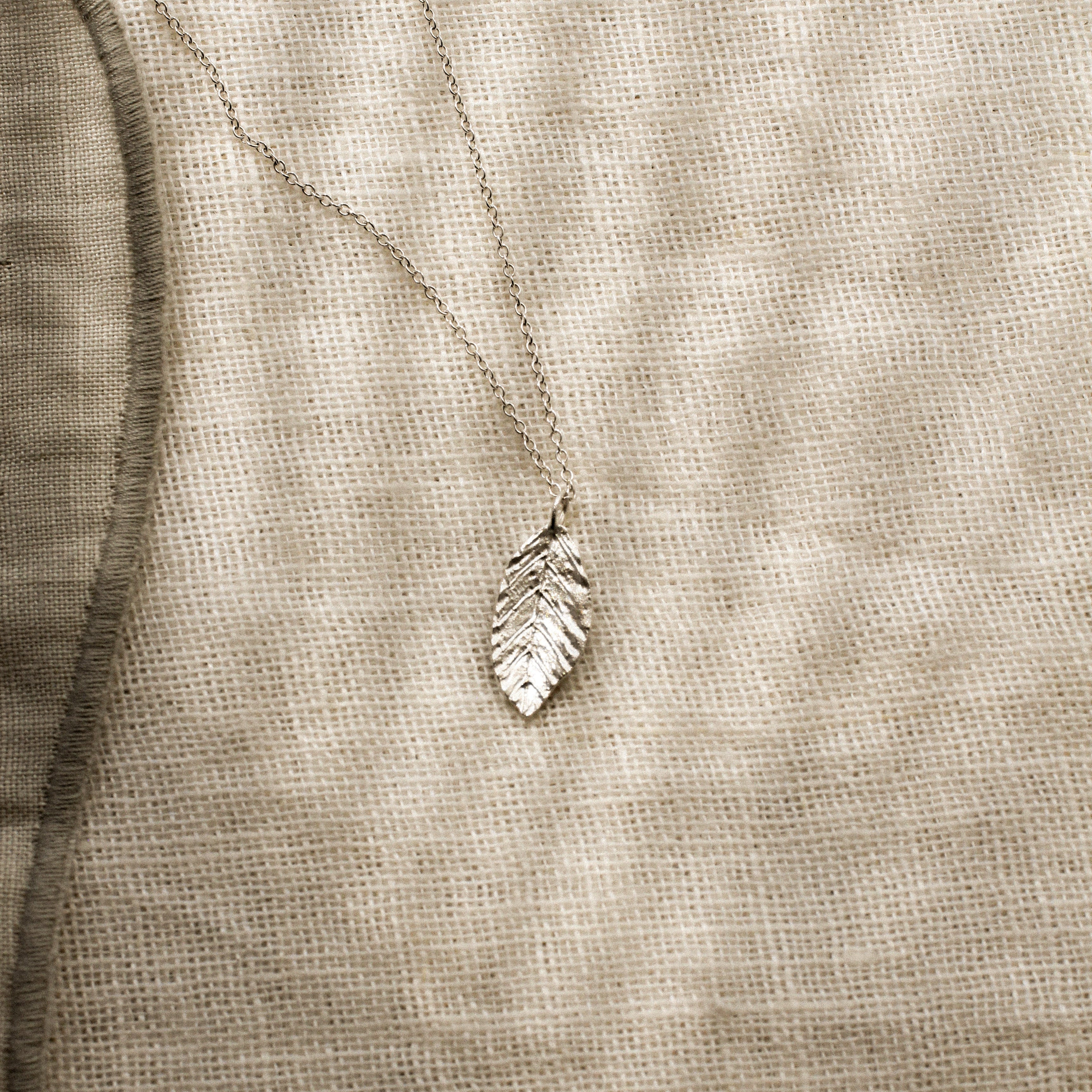 Silver leaf-shaped pendant on a beige fabric background