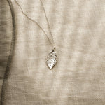 Silver leaf-shaped pendant on a beige fabric background
