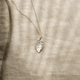 Silver leaf-shaped pendant on a beige fabric background
