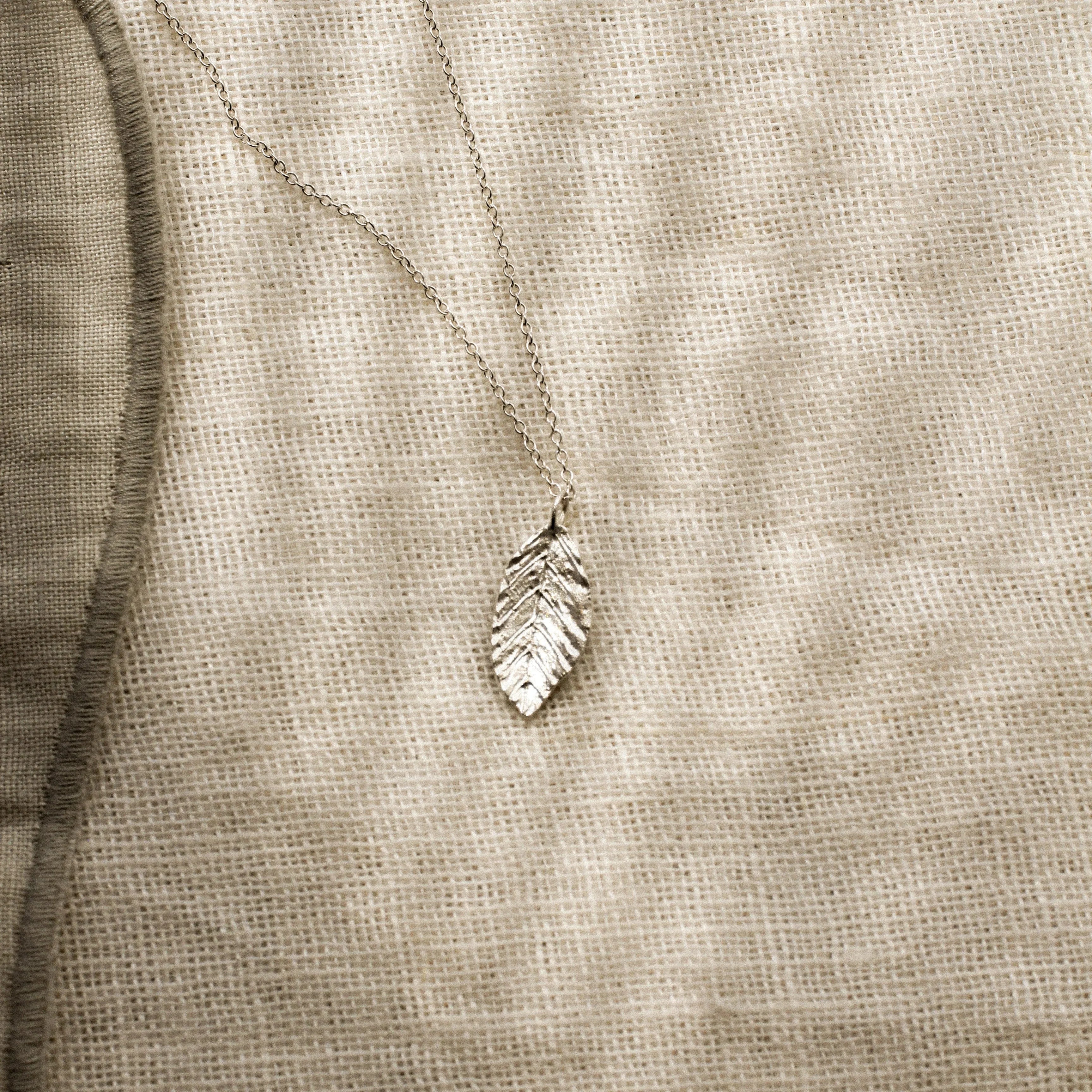 Silver leaf-shaped pendant on a beige fabric background