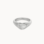 A textured silver ring with a heart-shaped face, photographed on a clean, solid off-white background.