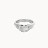 A textured silver ring with a heart-shaped face, photographed on a clean, solid off-white background.