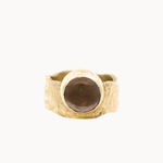A textured gold signet-style ring with a large, smooth, round brown stone, photographed against a solid off-white background.