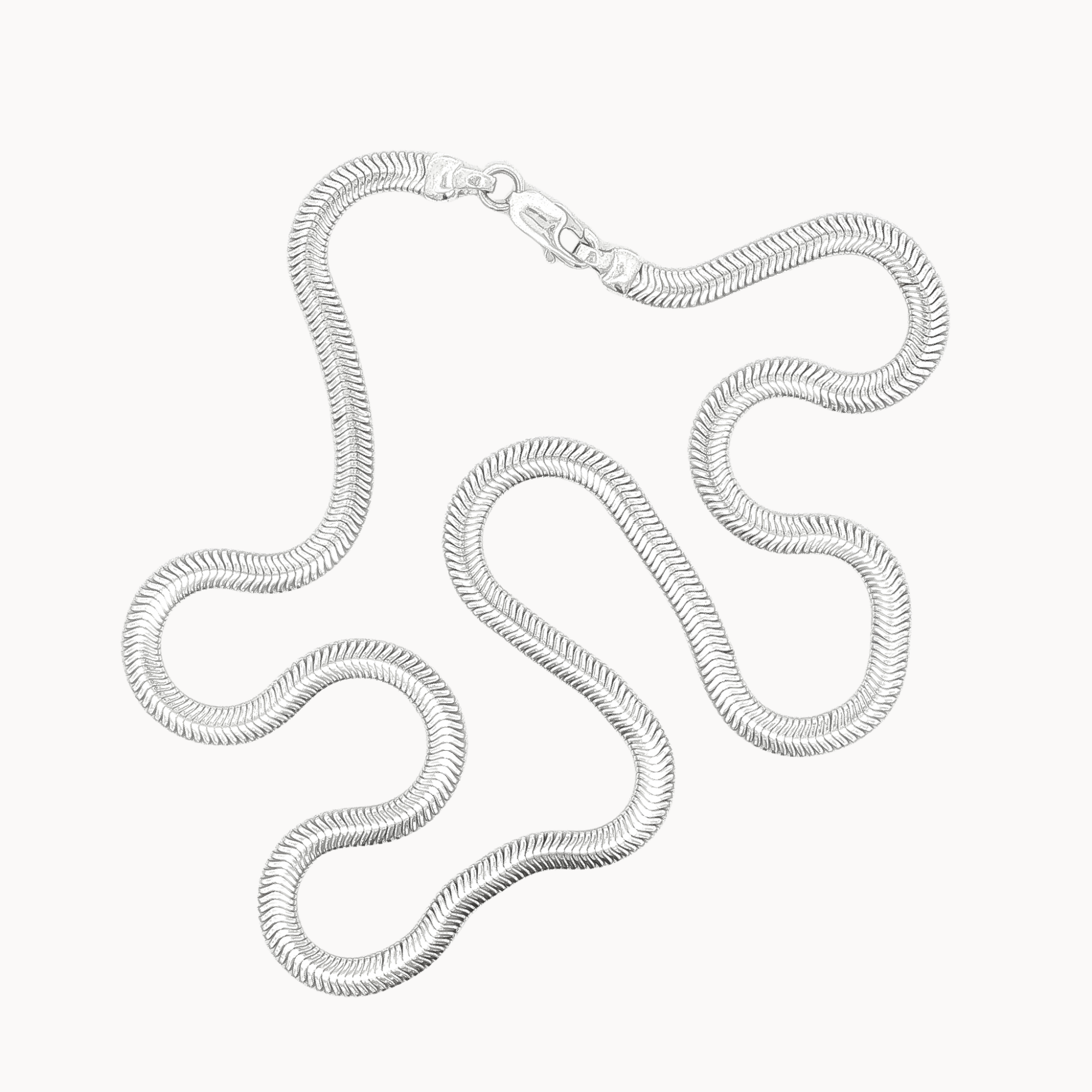 A silver-toned snake chain necklace with a lobster clasp, arranged in a loose loop on a plain off-white background.