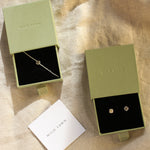 Jewelry set with sun bracelet and studs in green boxes with 'WILD LAWN' branding on a beige fabric background