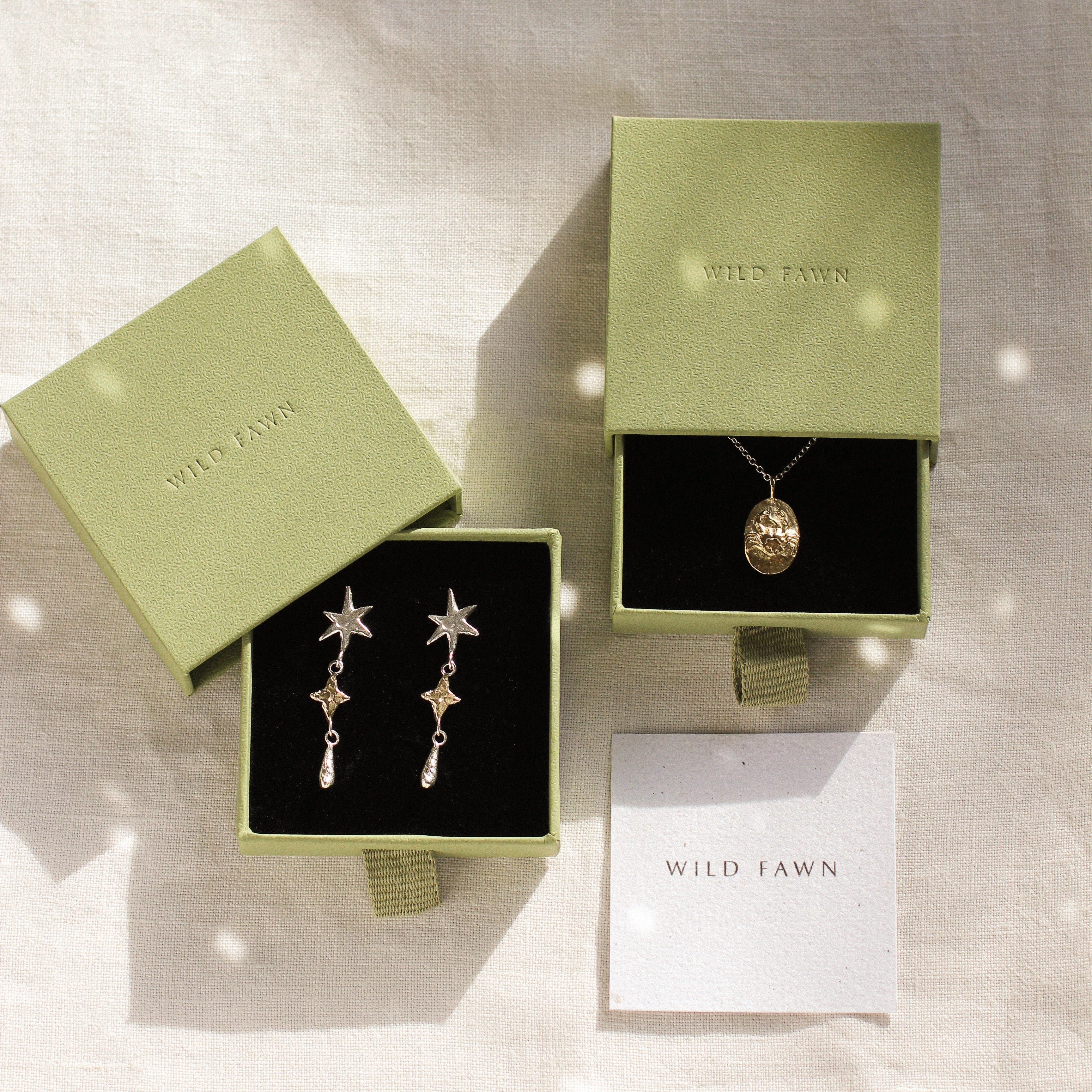 gold cancer zodiac necklace and star earrings in gold gift boxes on a neutral fabric