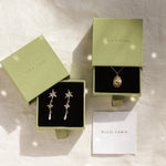 gold cancer zodiac necklace and star earrings in gold gift boxes on a neutral fabric