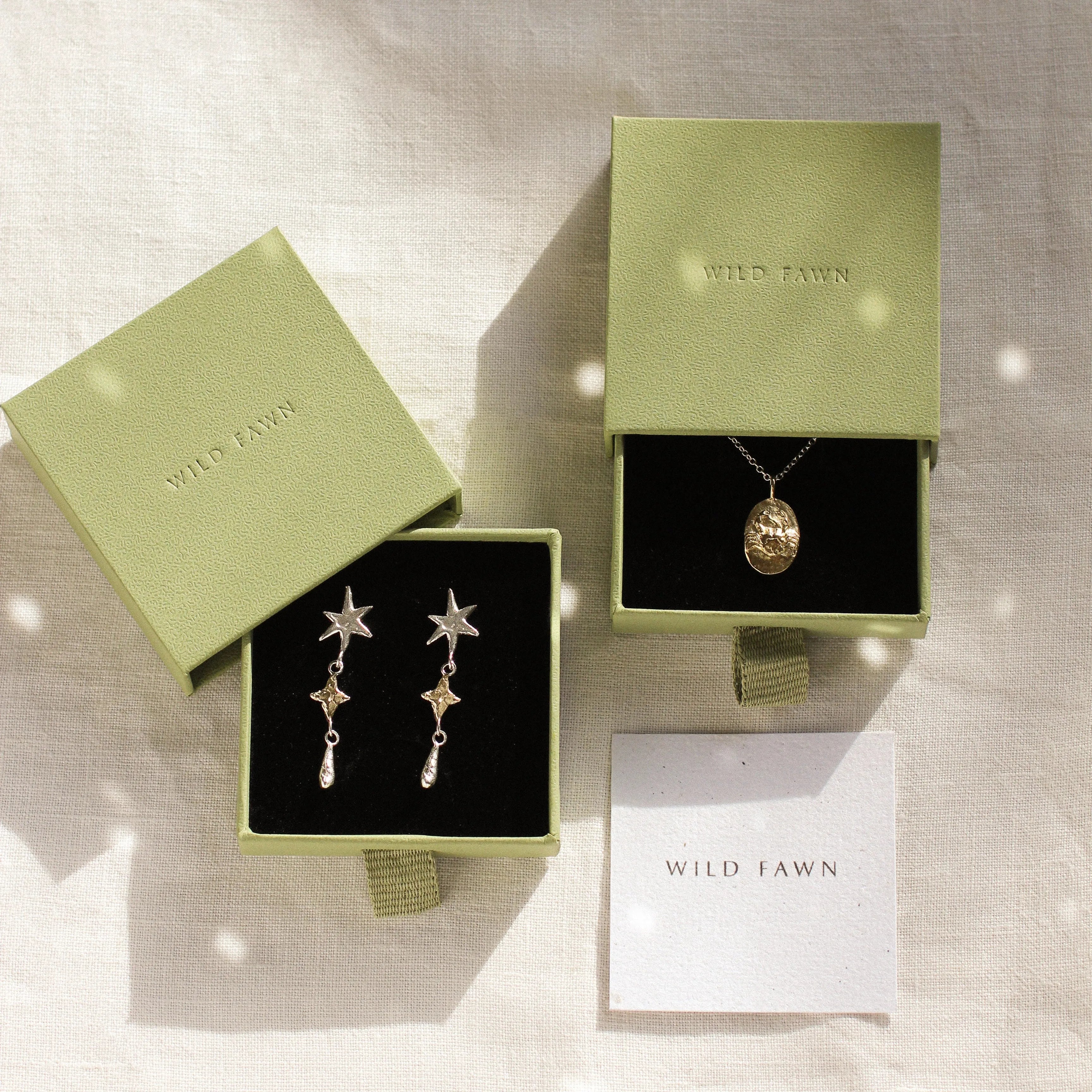 gold cancer zodiac necklace and star earrings in gold gift boxes on a neutral fabric
