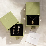 gold gemini necklace and shooting star dangle earrings in green boxes and wild fawn care card