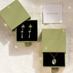 Jewelry set with earrings and a leo necklace in 'Wild Fawn' green boxes on a textured surface.