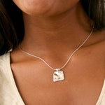 close up of a square textured pendant necklace on a silver snake chain worn on a womans chest