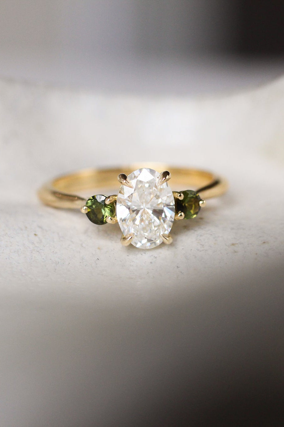 Gold ring with a diamond and green gemstones on a textured surface