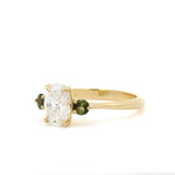 Gold engagement ring with a large diamond and smaller green gemstones on a white background