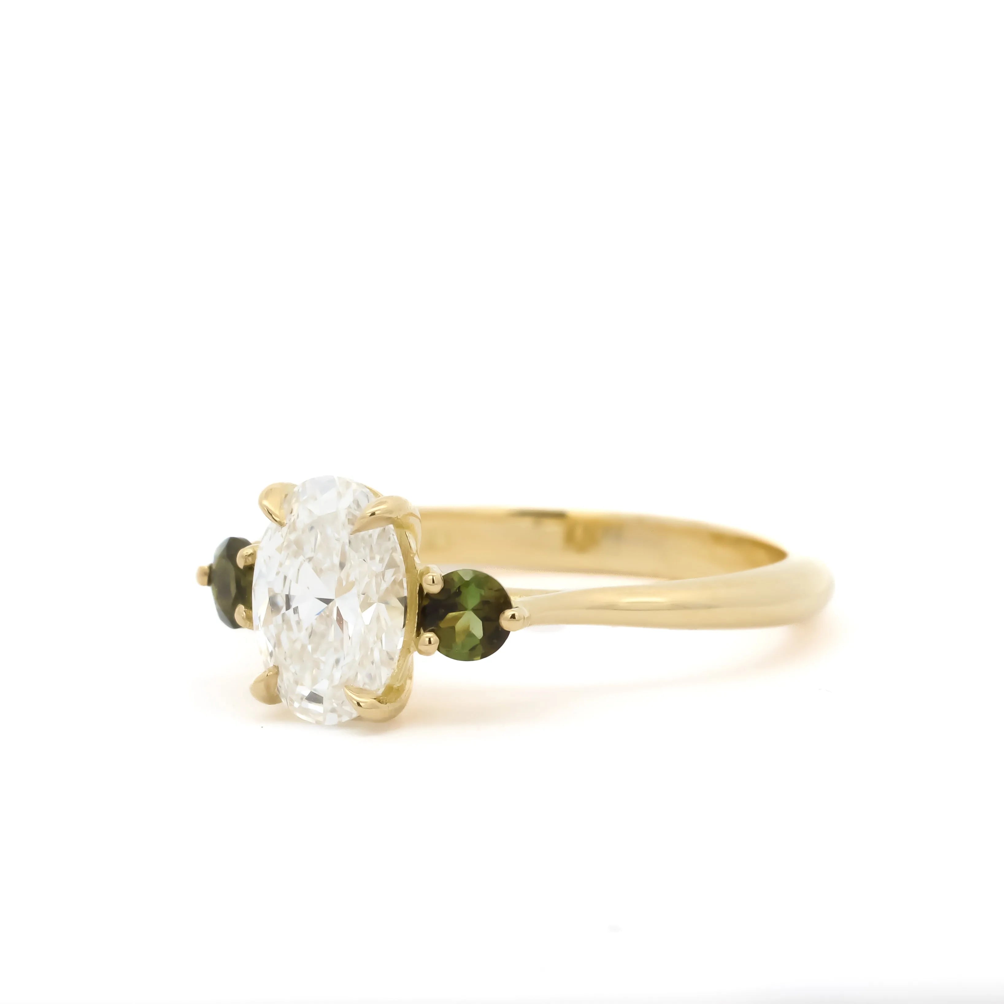 Gold engagement ring with a large diamond and smaller green gemstones on a white background