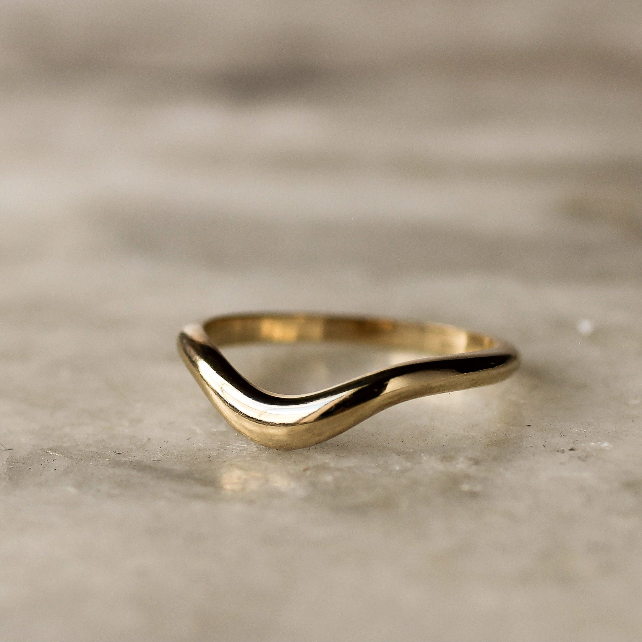 gold tapered curve wedding band on a marble surface