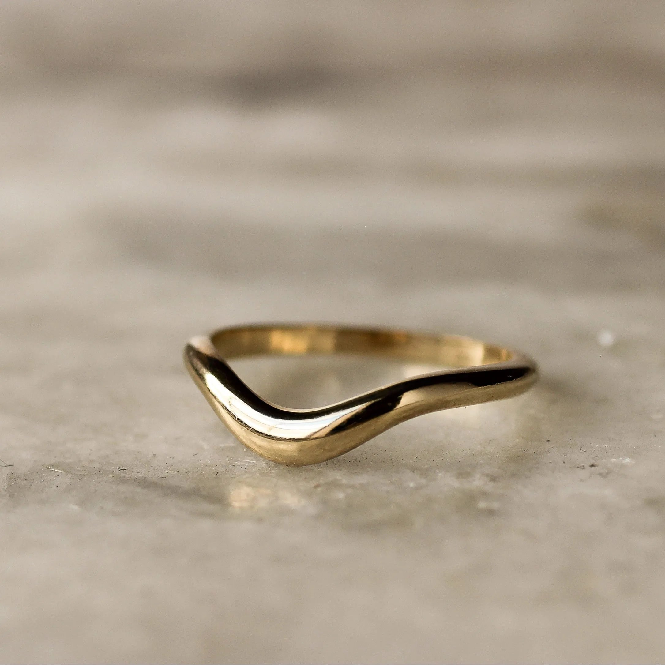 gold tapered curve wedding band on a marble surface