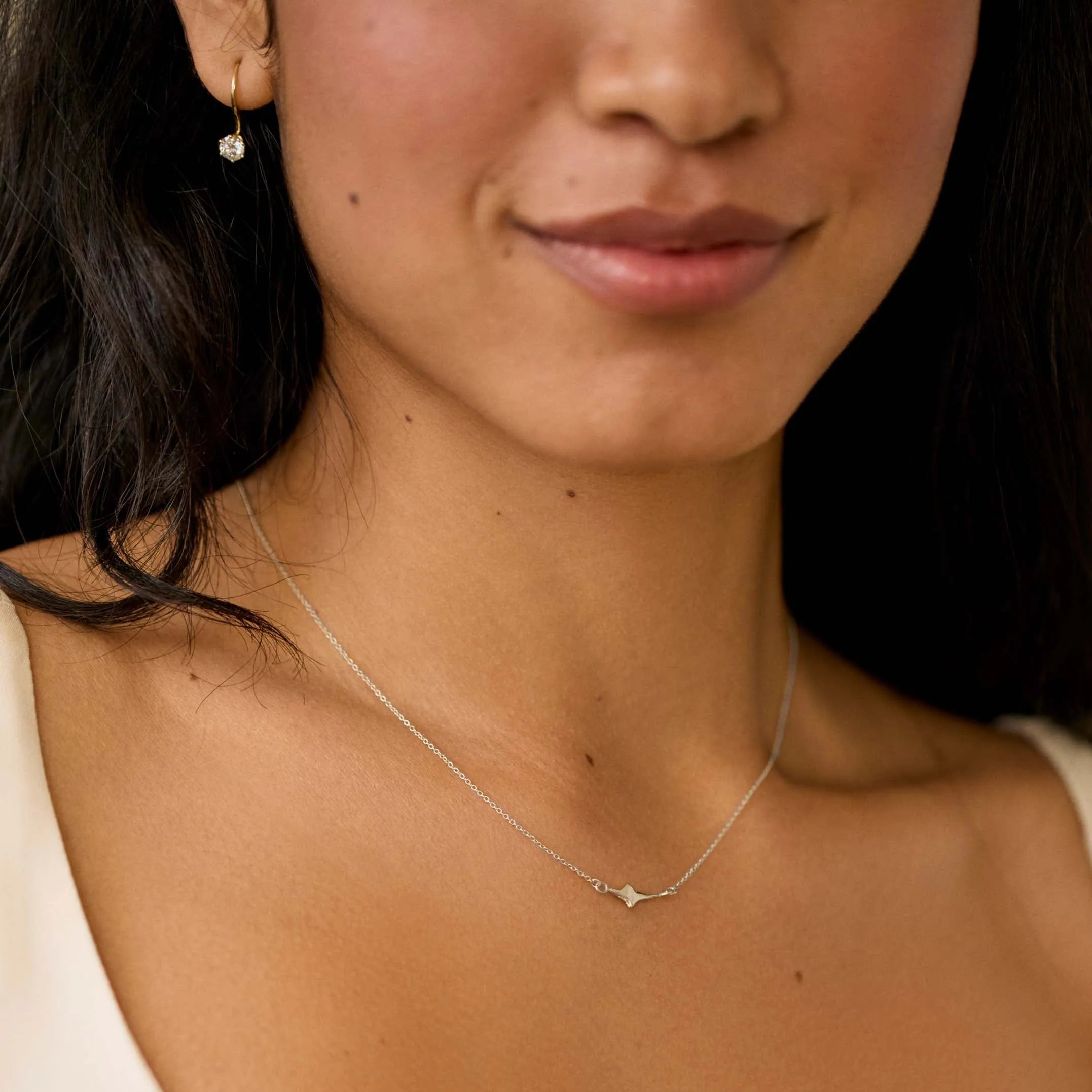 close up of woman wearing white gold tiny star necklace with diamond earrings