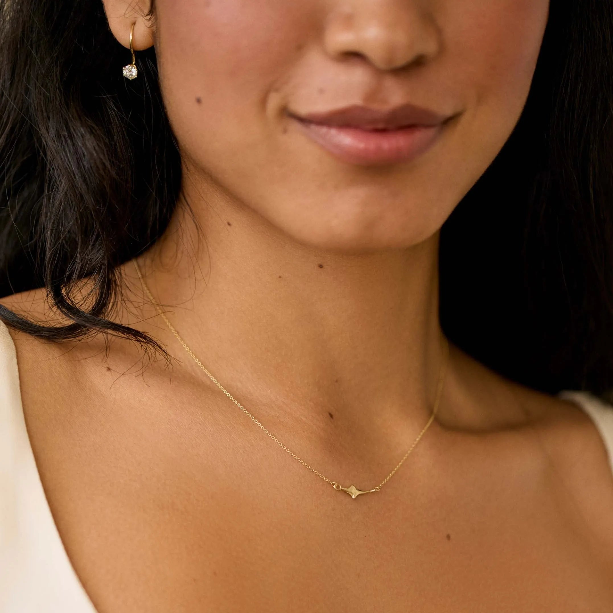 close up of woman wearing small gold star necklace on fine gold chain and diamond earrings