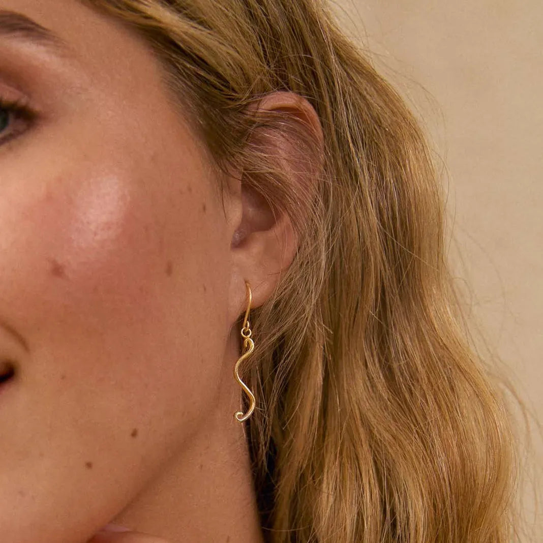 close up of a womans ear wearing a s-shaped dainty dangle earring