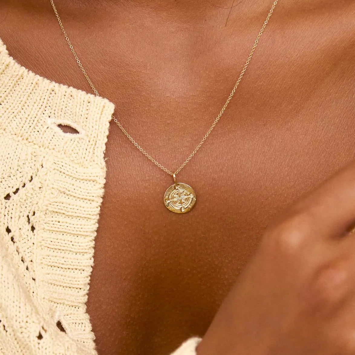 close up of a gold pendant necklace with compass design worn on a womans chest