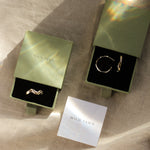 gold wave ring and wave hoops in green gift boxes with water reflection and wild fawn care card