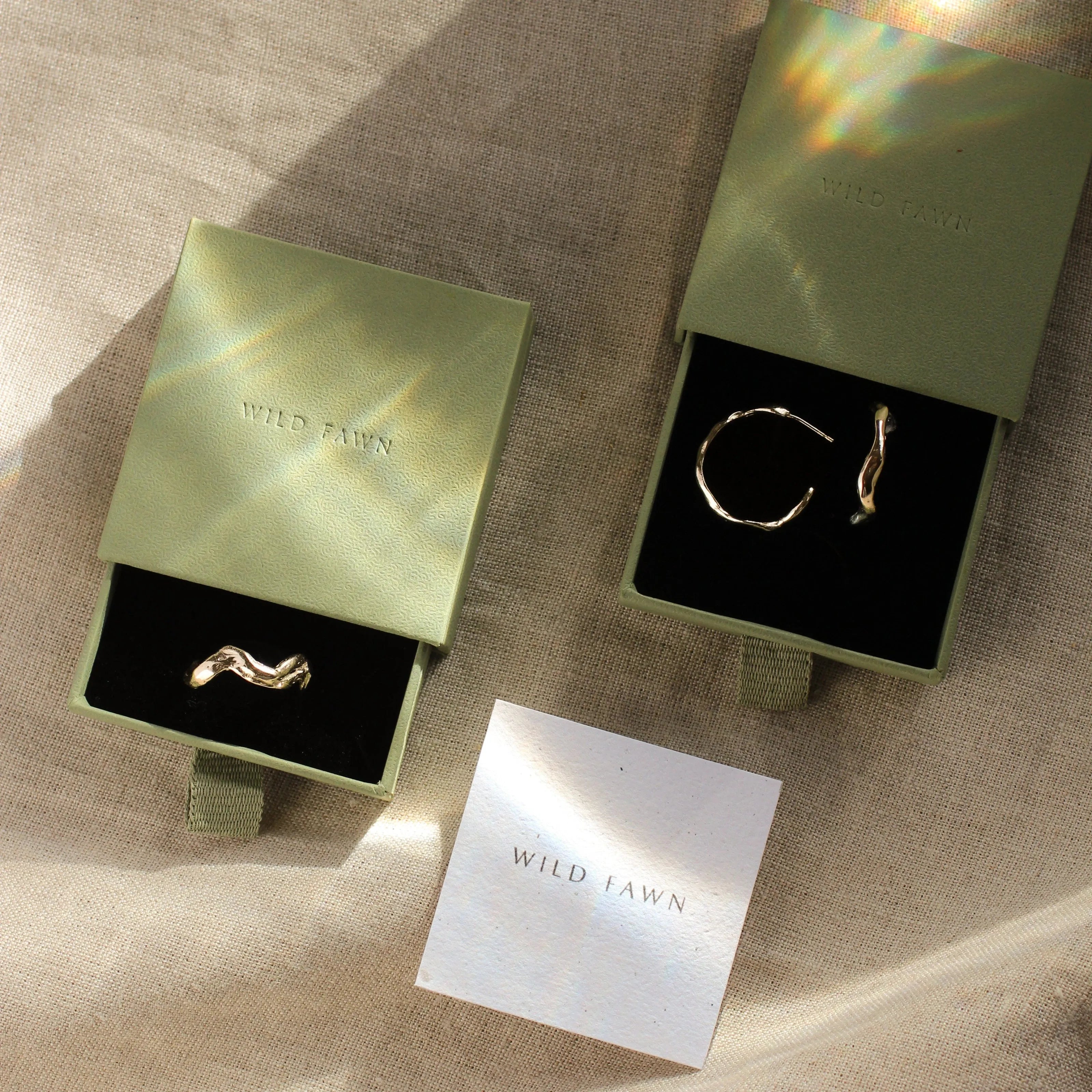 gold wave ring and wave hoops in green gift boxes with water reflection and wild fawn care card