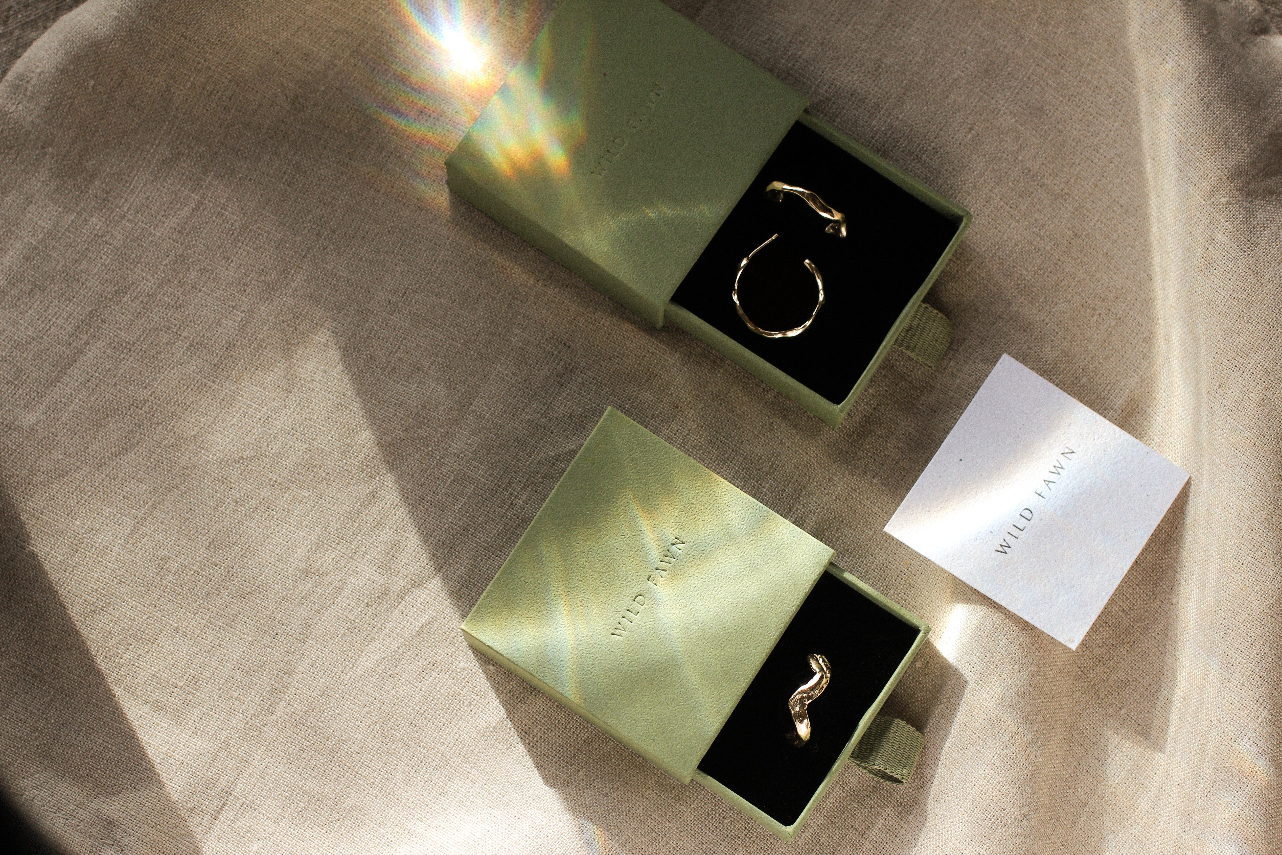 Gold earrings in a green jewelry box on a beige fabric background