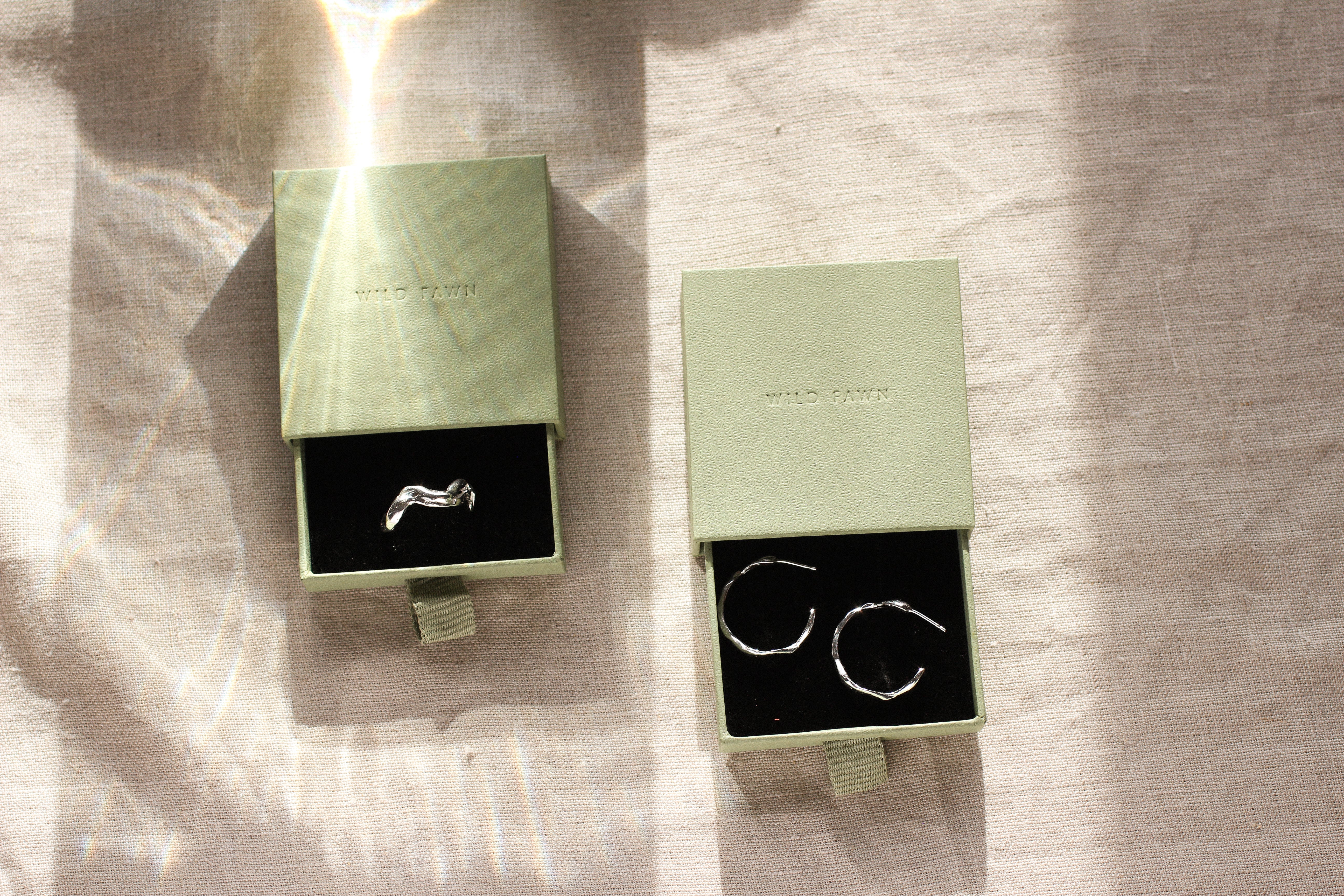 a pair of earrings and a wavy ring in open green boxes on a textured surface.