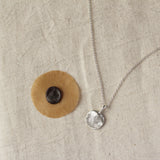 wax with fingerprint imprint next to a silver necklace with round pendant and fingerprint texture on a neutral fabric