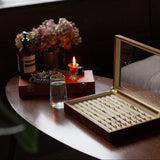 Wooden table with jewelry box, glasses, and flowers in a softly lit room.