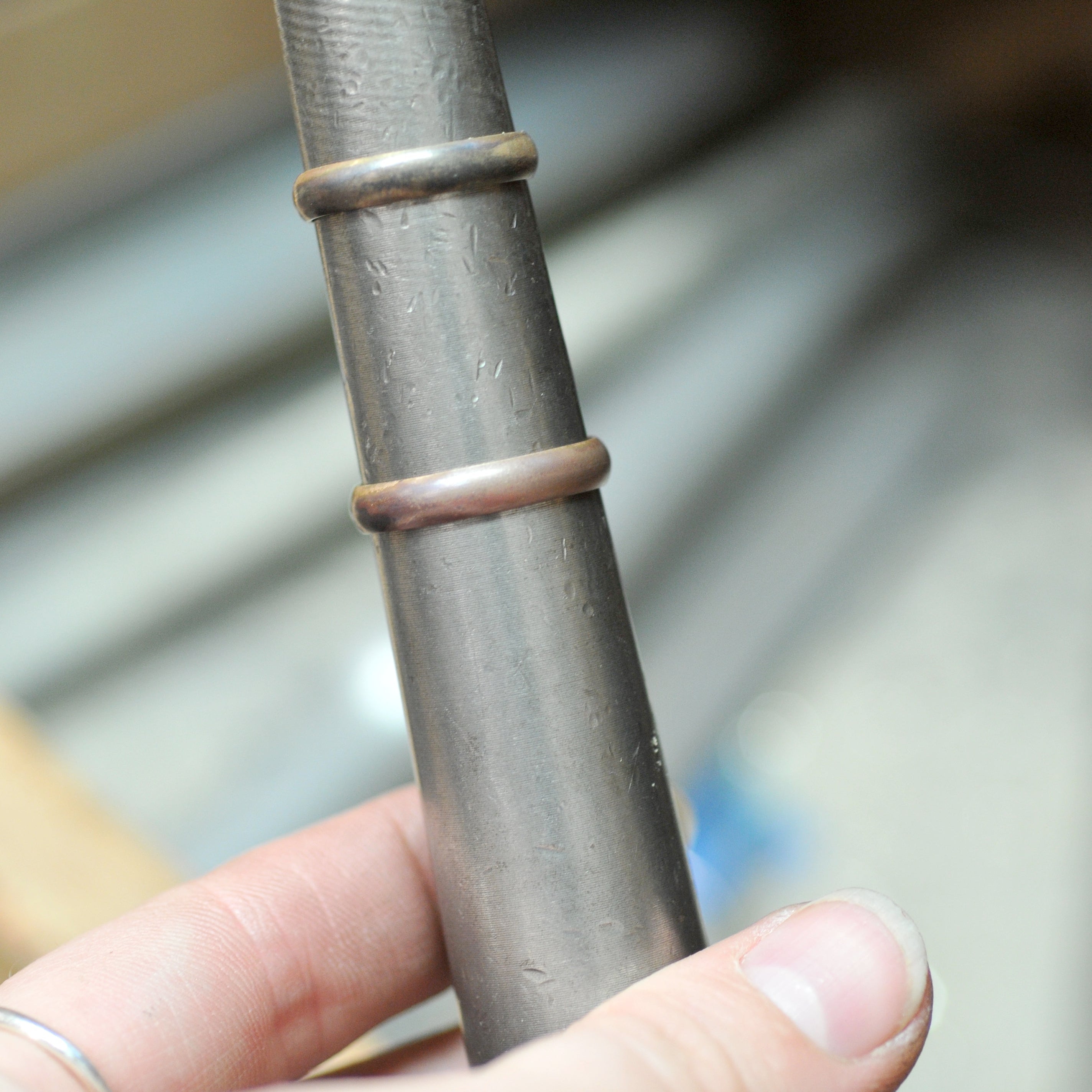 hands holding a ring mandrel with wo wedding bands on it